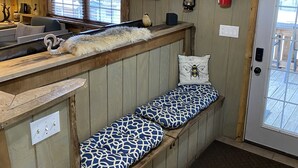 Un interior de cabaña acogedor con un banco de madera, un extintor y una ventana con persianas.