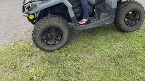 A person riding a four-wheeled ATV on a grassy area with a house and parked cars in the background. - Light and Airey new apartment on Apple Orchard minutes from Sylvan Beach (Blossvale)