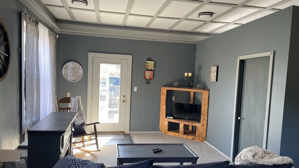 A living room with a sofa, coffee table, TV stand, and a door leading outside. - Light and Airey new apartment on Apple Orchard minutes from Sylvan Beach (Blossvale)