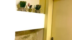 A door with a metal handle, a white shelf above it with potted plants, and a wall with exposed brickwork. - RoadHouse (Wadi Musa)