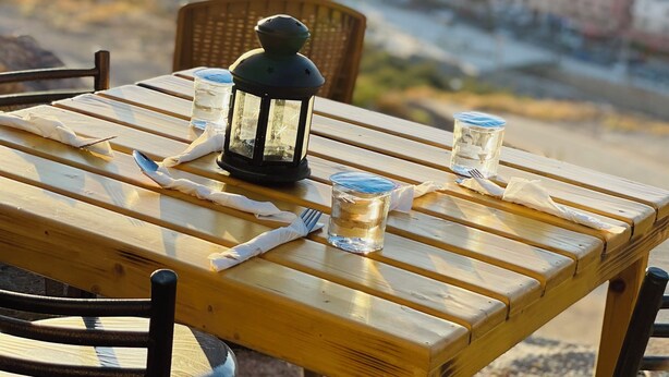 A wooden table with a lantern, a glass, and a napkin. The table is outdoors with a view of a city and mountains in the background. - RoadHouse (Wadi Musa)
