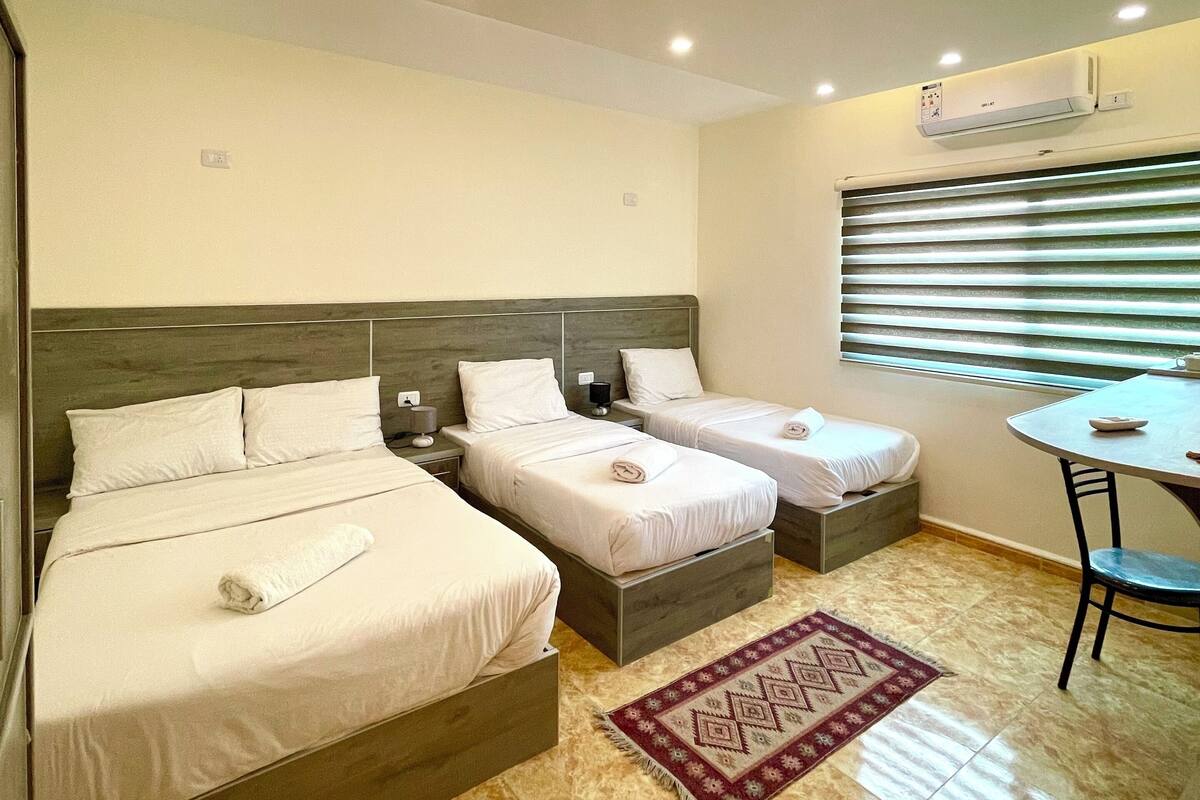 Quarto de hotel com duas camas, uma mesinha e janela com persianas.