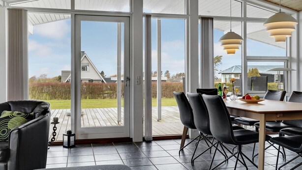 A spacious room with a large sliding glass door leading to an outdoor deck. Inside, there is a dining table with chairs, a small coffee table, and a potted plant.