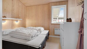 A bedroom with a wooden interior, a bed with white bedding, a window with a view, and a white refrigerator.