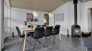 A modern dining area with a wooden table and black chairs, a black wood-burning stove, and pendant lights.