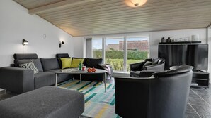A modern living room with a grey sofa, a black armchair, and a coffee table. There is a large window with a view of a garden and a house.