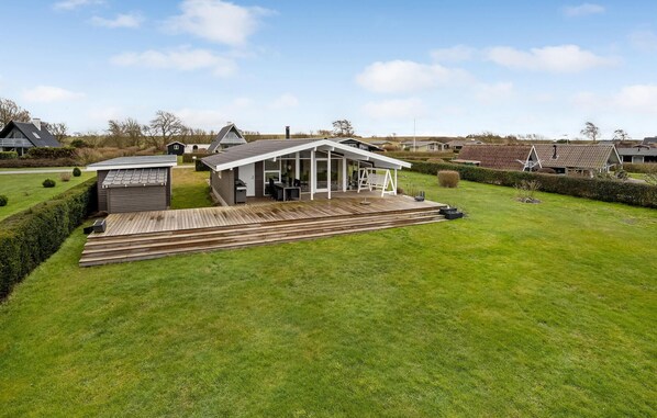 A modern house with a large deck, a covered outdoor area, and a well-maintained lawn.