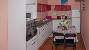 Una cocina compacta con armarios blancos, un microondas, una cafetera y un refrigerador. Hay una mesa de comedor con sillas y un jarrón con flores.