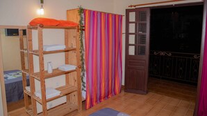 Una habitación con una litera de madera, una cortina a rayas y una puerta que da a un balcón.