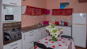 Una cocina compacta con armarios blancos, un microondas, un refrigerador y una zona de comedor con una mesa preparada para dos personas.