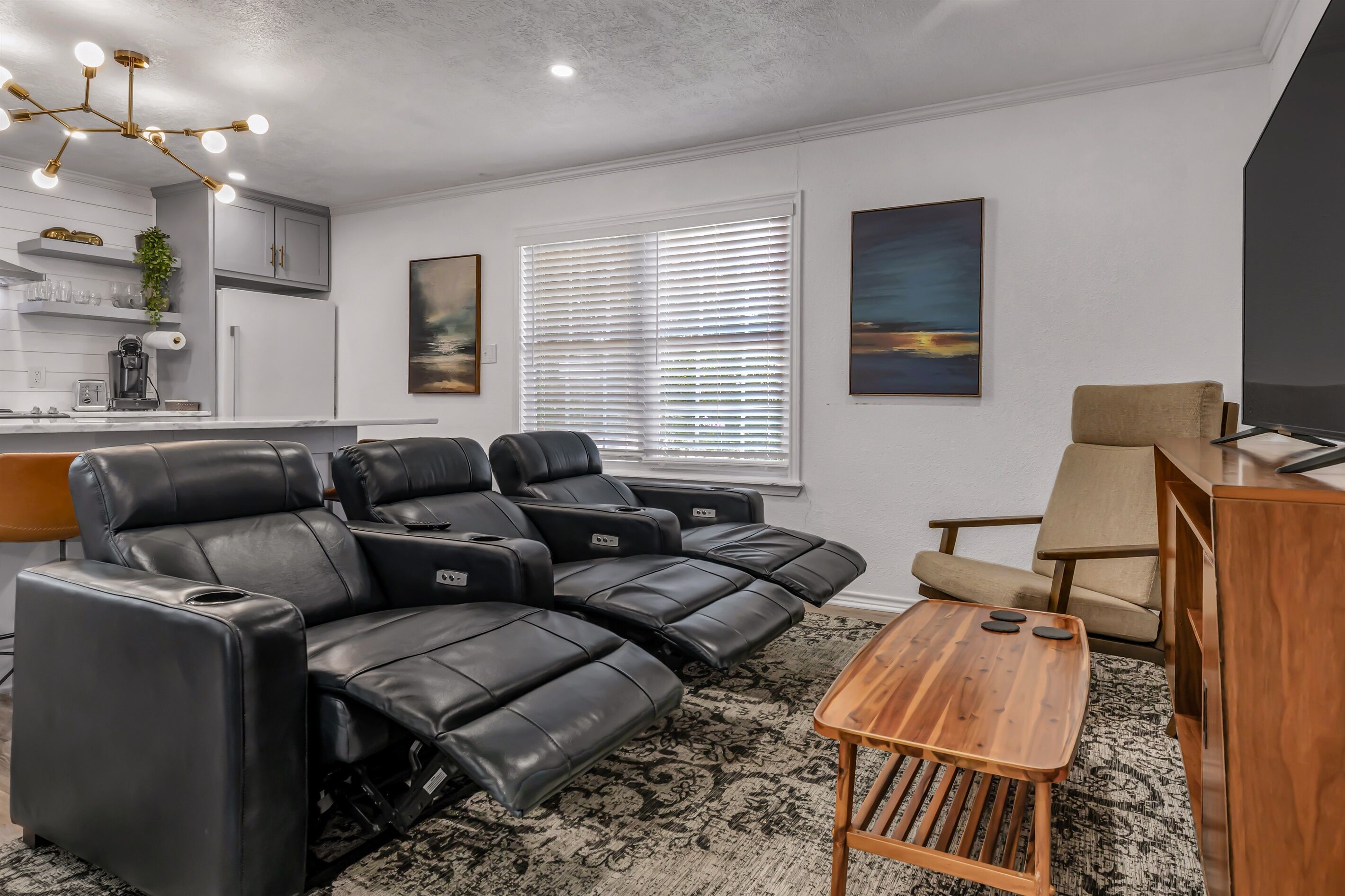 Una sala moderna con un sofá modular, un sillón reclinable, una mesa de centro de madera y un televisor.