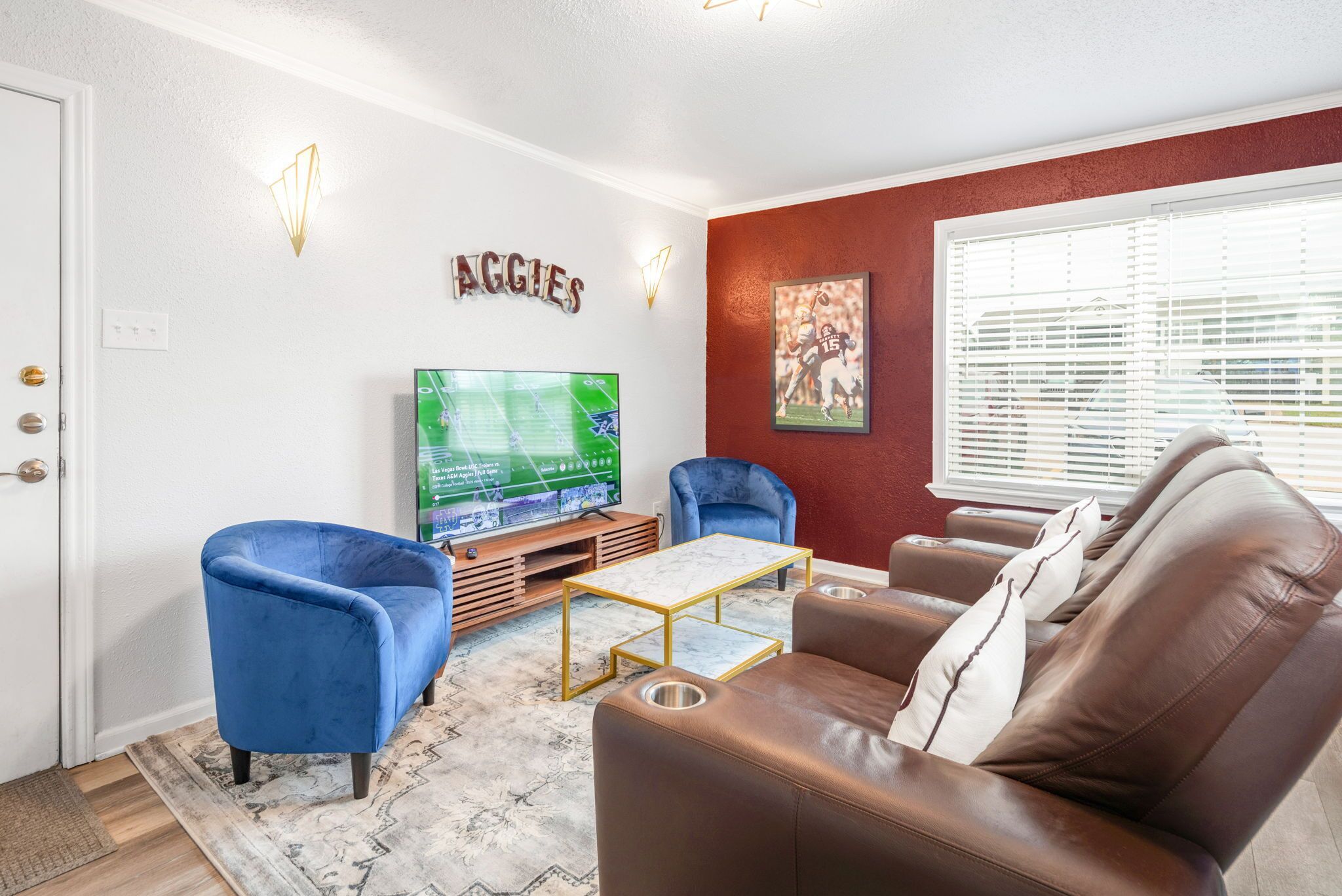 A living room with a TV, blue armchair, brown leather sofa, and a red accent wall.
