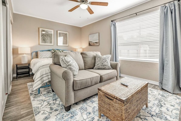 A bedroom with a bed, a sofa, a wicker coffee table, and a ceiling fan.