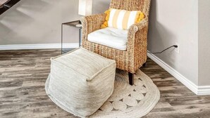 A cozy room with a wicker chair, a small ottoman, a lamp, and a framed picture on the wall. - St Simons: 3 Bedroom, Walk to A&M, King Beds (Bryan)