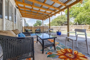 A covered patio area with outdoor furniture, a glass table, and a decorative rug.
