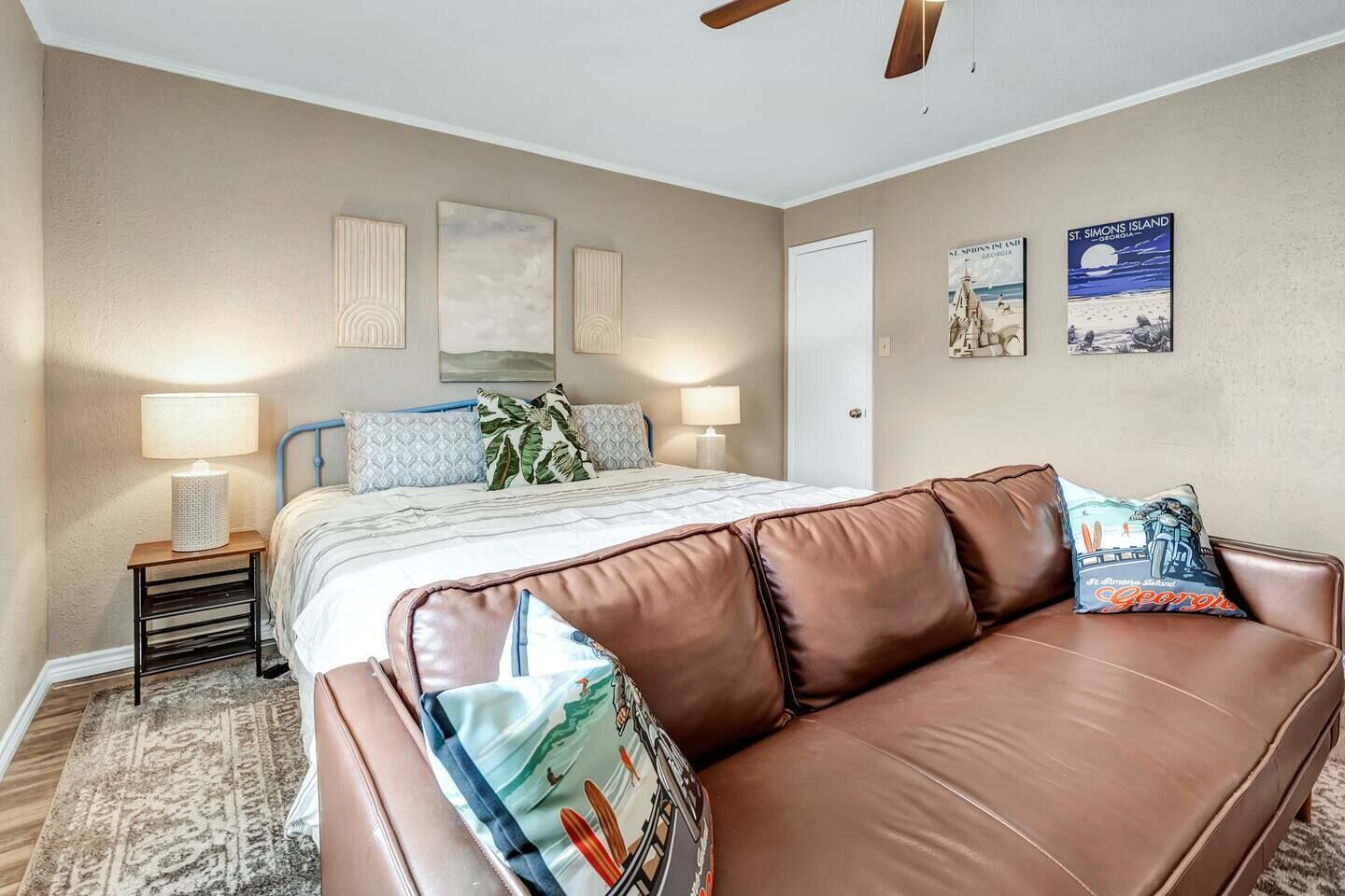 Quarto com cama, sofá de couro marrom, mesa de cabeceira com abajur e decoração na parede.