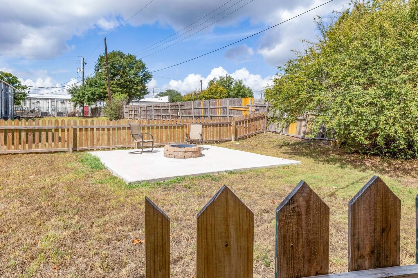 A backyard with a concrete patio, a fire pit, and a wooden fence.