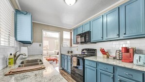 A kitchen with blue cabinets, a stainless steel sink, a microwave, a stove, and a red coffee maker. - St Simons: 3 Bedroom, Walk to A&M, King Beds (Bryan)