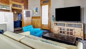 A living room with a beige sofa, a blue armchair, a wooden cabinet with a TV, and a wooden door with a window. - Starry Night: Dwntwn Bryan on Main St, 2nd Flr, King Bed (Bryan)
