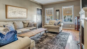 Un salon avec un canapé beige, un fauteuil assorti, une table basse en bois et un tapis à motifs.