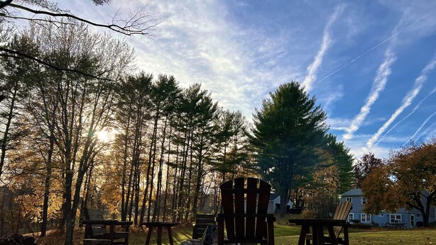 A serene outdoor seating area with wooden chairs and tables, surrounded by trees and a clear sky.