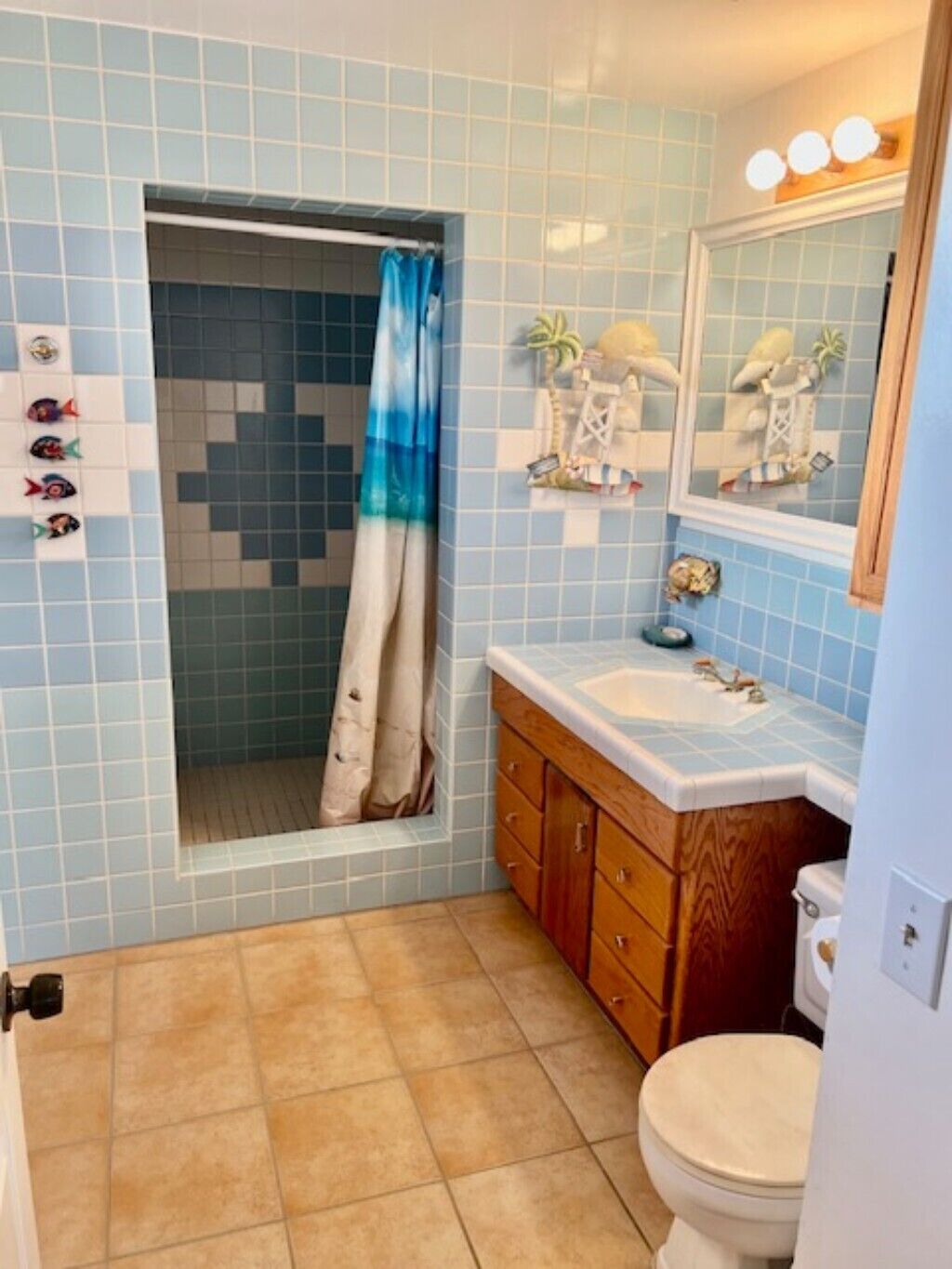 Badeværelse med blå fliser, en trævasketøj og et toilet samt en bruseniche med blå og hvid gardin.