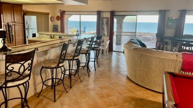 A spacious living area with a kitchen, bar area, and a large window offering a view of the ocean. - Beachfront House on Beautiful Laguna Percebu Beach (San Felipe)