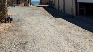 A gravel driveway leading to a building with a solar panel on the roof, a covered area with a chimney, and a view of the sea. - Beachfront House on Beautiful Laguna Percebu Beach (San Felipe)