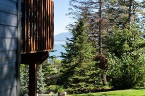 A view of a house with a wooden deck, surrounded by lush greenery and a lake.