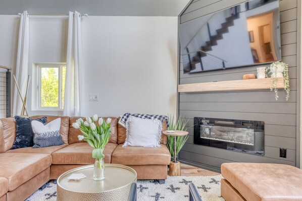 Una sala de estar moderna con un sofá modular, una mesa de centro redonda, una chimenea y un televisor montado en la pared.