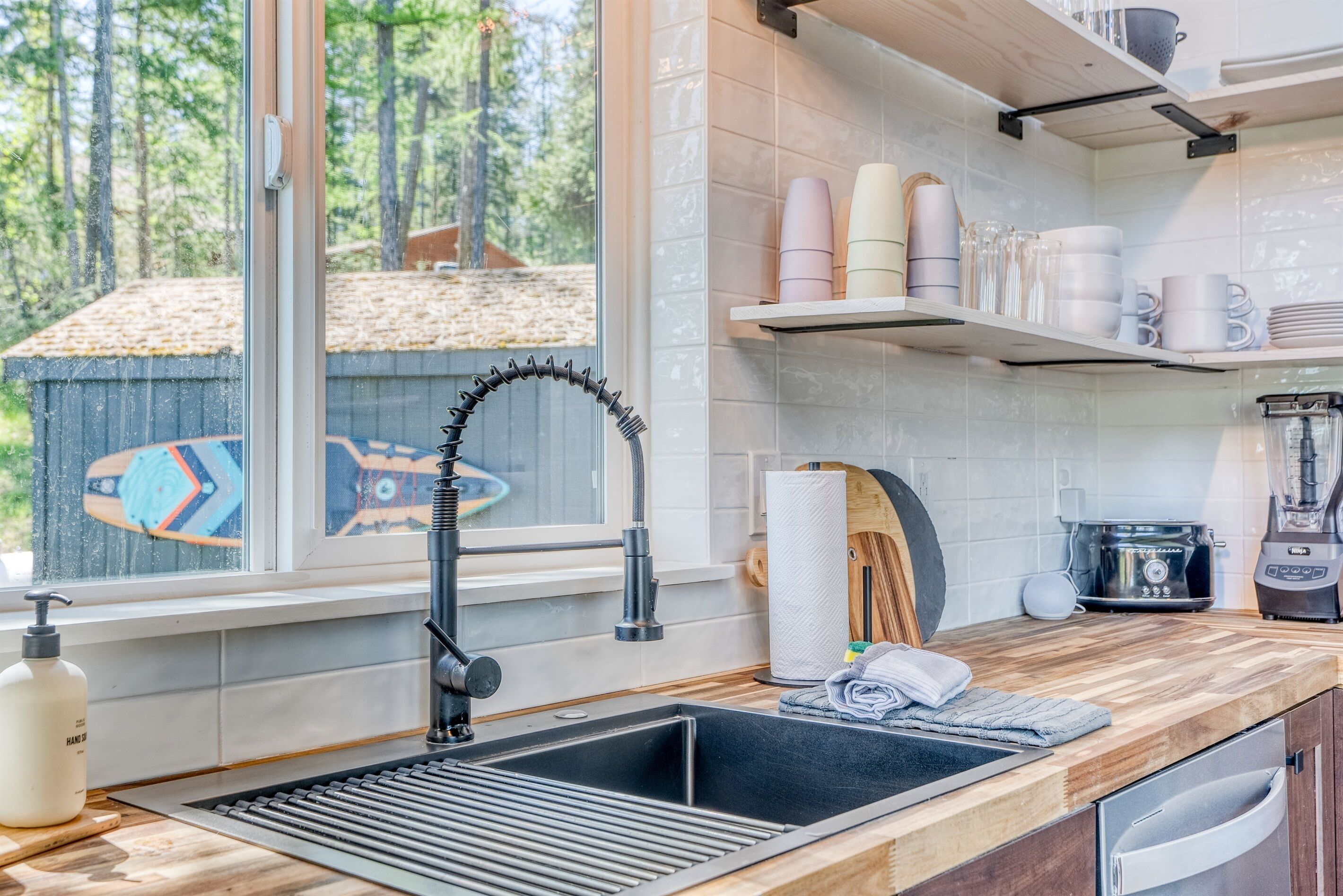 A modern kitchen with a large window, wooden countertops, a stainless steel sink, and a blender on the counter.