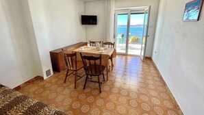 A dining area with a table and chairs, a television on the wall, and a view of the sea through a glass door. - Holiday apartment with a balcony and sea view (Dramalj)