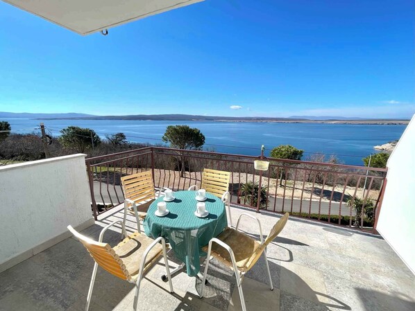 A balcony with a table and chairs, overlooking a scenic view of the sea and hills. - Holiday apartment with a balcony and sea view (Dramalj)