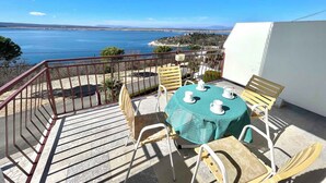 A balcony with a table and chairs, overlooking a body of water and a distant landscape. - Holiday apartment with a balcony and sea view (Dramalj)