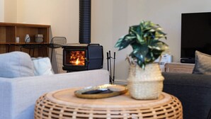 Ein gemütliches Wohnzimmer mit Kaminofen, Fernseher und bequemen Sitzmöglichkeiten.
