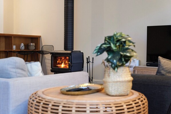A cozy living room with a wood-burning stove, a television, and comfortable seating. - Historic Battery Point Cottage (Battery Point)