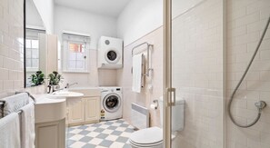 A compact, modern bathroom with a checkered floor, a washing machine, a toilet, and a shower. - Historic Battery Point Cottage (Battery Point)