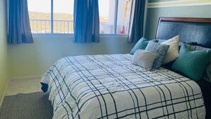 A bedroom with a bed, curtains, a headboard, and a window with a view of a building.