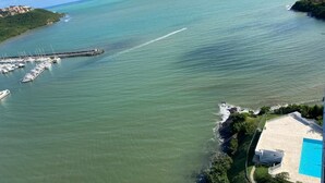 An aerial view of a coastal area with a marina, a swimming pool, and a building with a balcony overlooking the water.