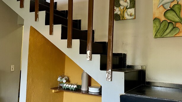 Un escalier avec une rampe en bois menant à un espace cuisine équipé de casseroles et d’une machine à café.