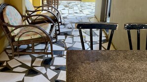 Une pièce avec un sol carrelé, une table entourée de chaises, une porte et un mur orné d’un tableau.