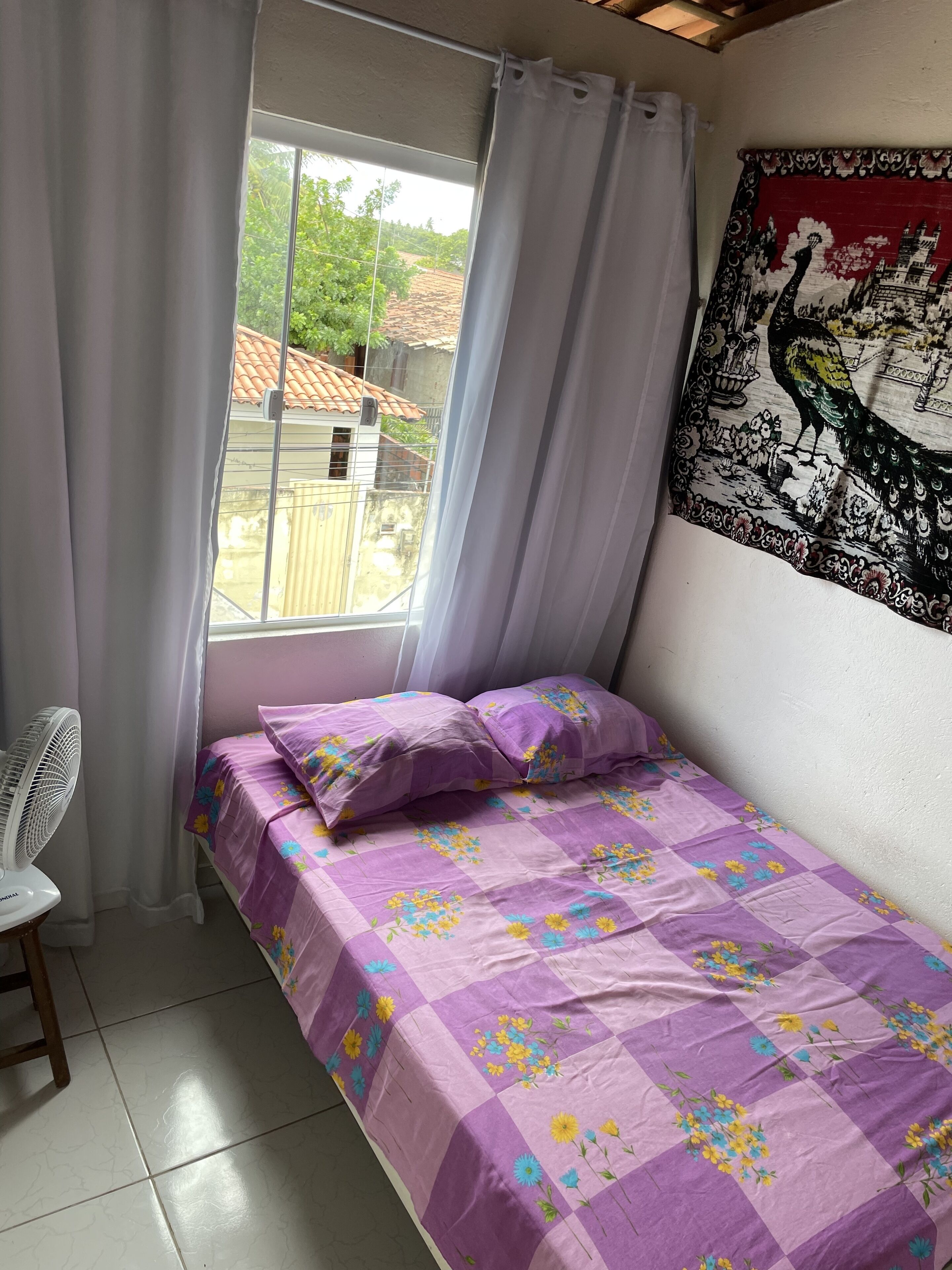 A bedroom with a bed, a fan, and a window with curtains.