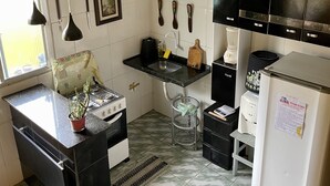Une cuisine de taille réduite, équipée d’une cuisinière à gaz, d’un évier, d’un réfrigérateur et d’un plan de travail agrémenté d’une plante en pot.