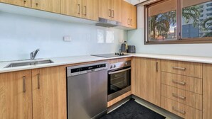 Eine moderne Küche mit Holzausstattung, einem Geschirrspüler, einem Backofen und einem Fenster mit Blick auf Palmen.