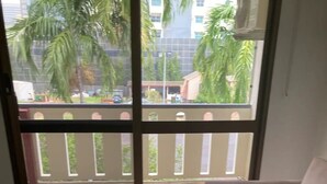Ein Wohnzimmer mit einem Glastisch, einem beigefarbenen Sofa und Blick auf einen Balkon mit Palmen und einem Gebäude im Hintergrund.