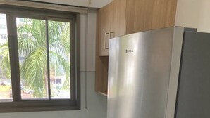 Eine Küche mit einem Edelstahl-Kühlschrank, Holzschränken und einem Fenster mit Blick auf Palmen.