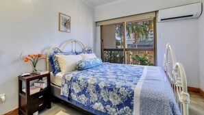 Ein Schlafzimmer mit einem Bett, einem Nachttisch, einem Fenster und einer Klimaanlage.