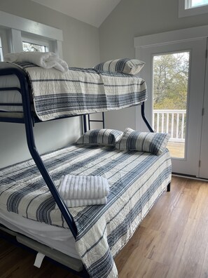 Ein Stockbett mit gestreifter Decke und Kissen, ein Holzboden und ein Balkon mit Geländer.