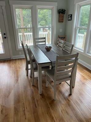 Ein Esszimmer mit Holztisch und -stühlen, großen Fenstern und Blick ins Freie.