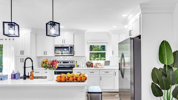 A modern kitchen with white cabinetry, stainless steel appliances, and pendant lighting.